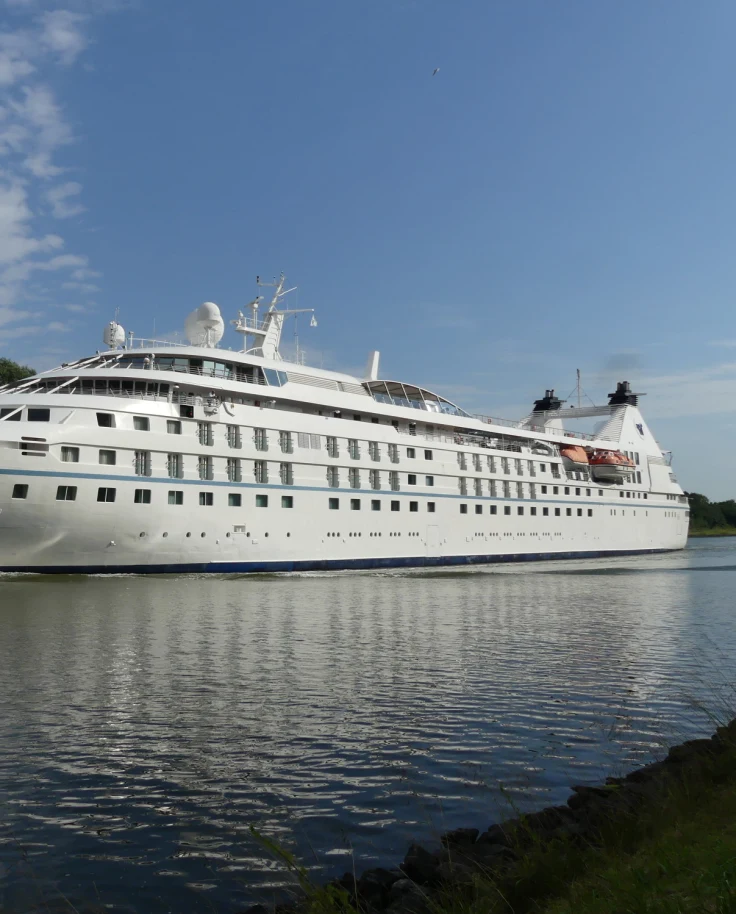 Windstar Cruises Star Legend Ship sits at port as the expansive vessel reflects in the water below on a sunny day.