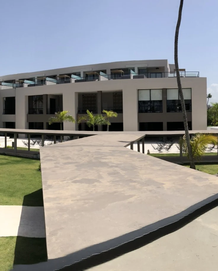 A panoramic view of a hotel exterior with palm trees, a path, grassy lawn and balcony.