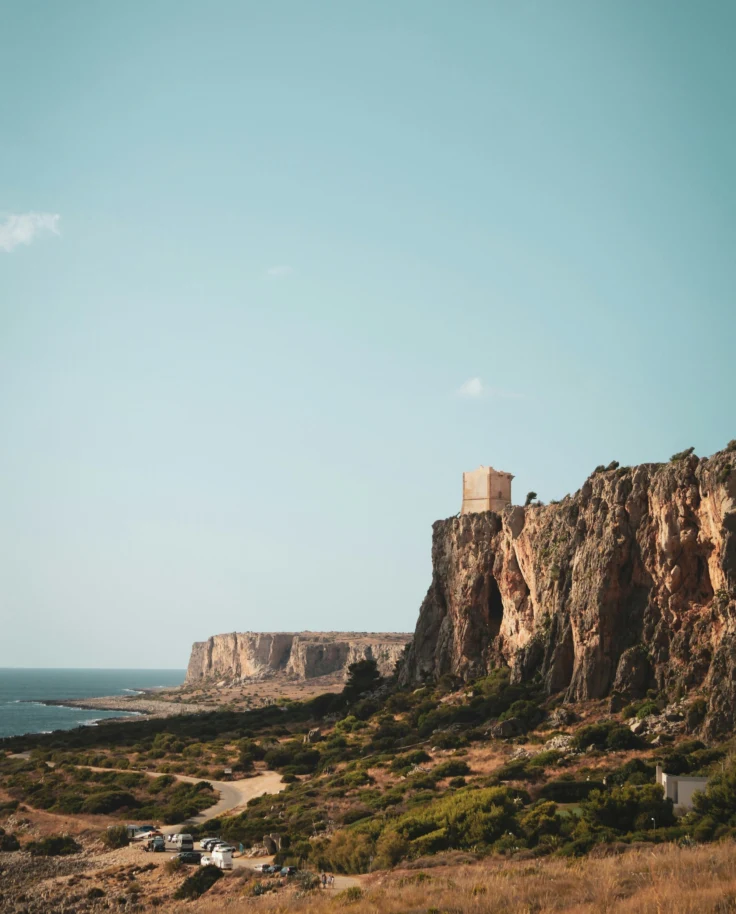 A view of striking cliffs and the ocean against a clear blue sky in Sicily.