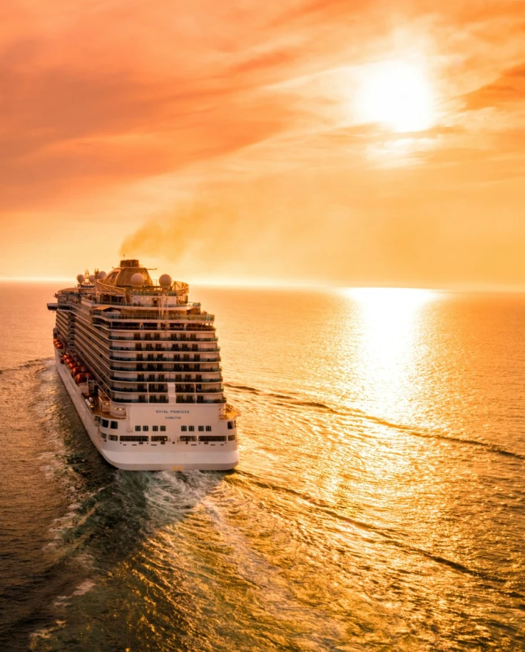 View of the cruise ship sailing towards the sunset on calm water.