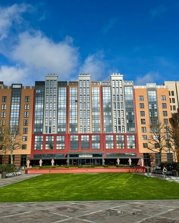 The exterior of Hotel New York – The Art of Marvel, the best hotel near Disney Paris, with tall red and orange towers behind a green lawn.