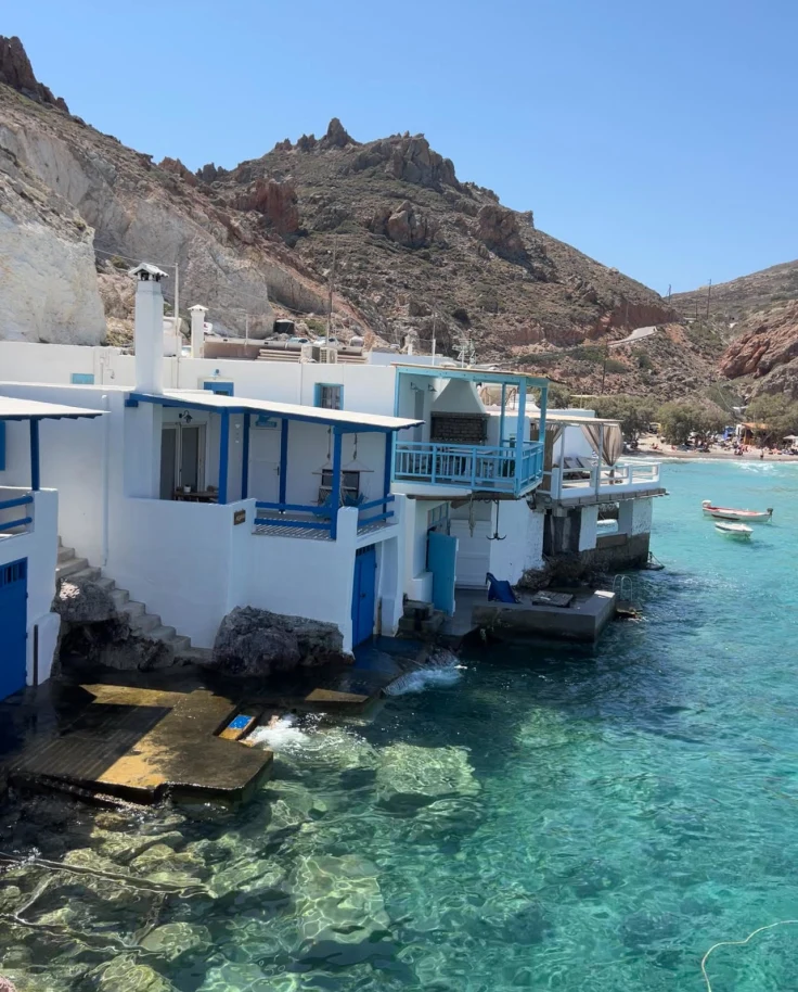 A view of traditional white and blue houses looking out to crystal-clear turquose waters in Greece.