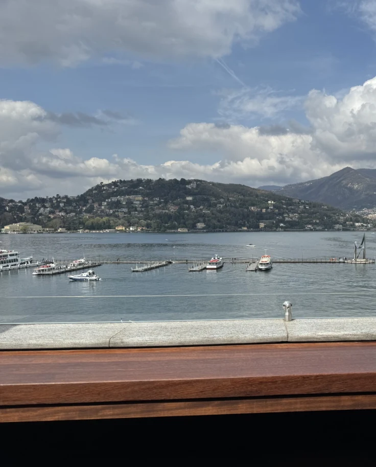 A photo of Lake Como with boats sailing across it and a mountain on each coast of the lake.