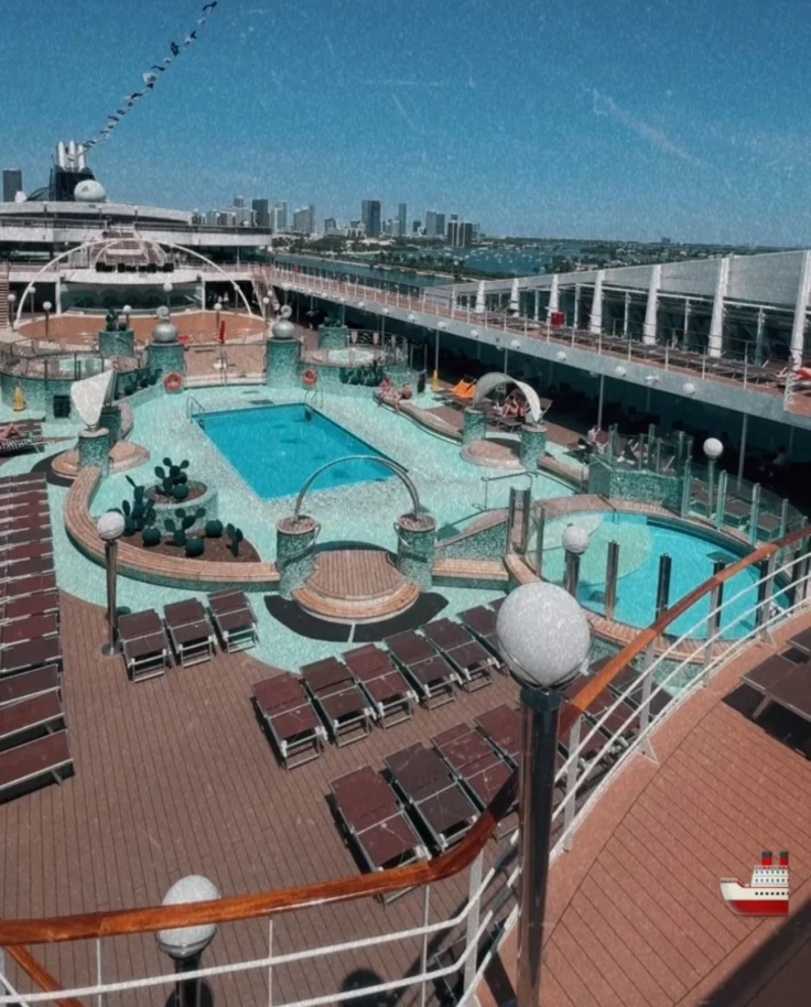 An aerial shot of a cruise ship's outdoor pool area with two pools, lounge chairs and shaded areas.