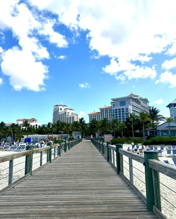 A point of view shot from a pier leading to the sandy shores before Baha Mar Hotel on a sunny day.