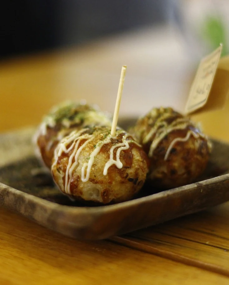 A wooden table with a plate of a savory balls of batter filled with diced octopus, a typical Osaka street food.