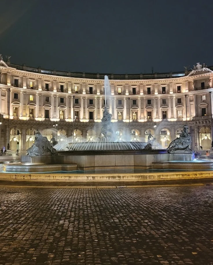 A fountain at night with a circular building behind it near one of the best hotels in Rome Italy for couples.