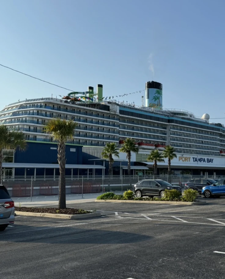 A large cruise ship docked at a port with a parking lot next to it during the daytime