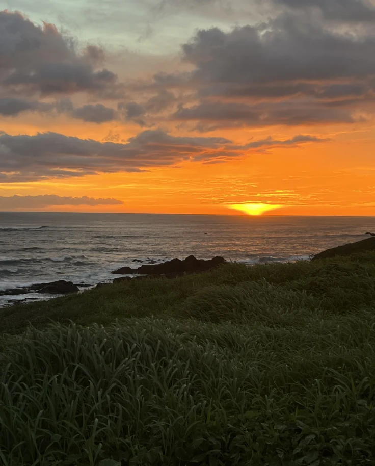 A blood-orange sunset over the sea and grassy land.