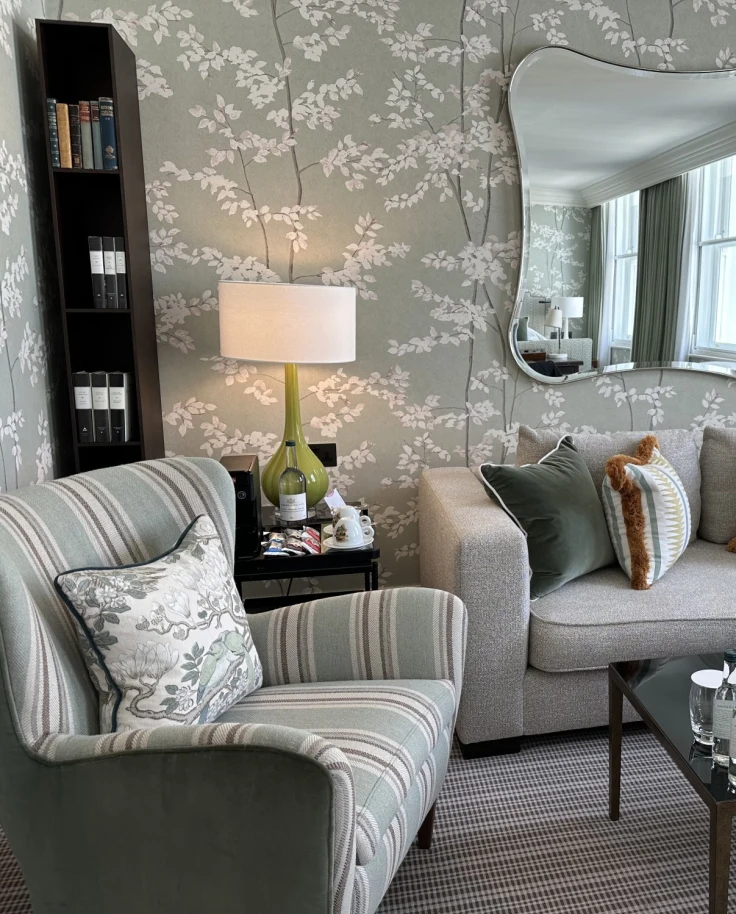 The sitting area of a suite at Brown's Hotel, London with gray and white flowery wallpaper, gray sofas with cushions and gray carpet.