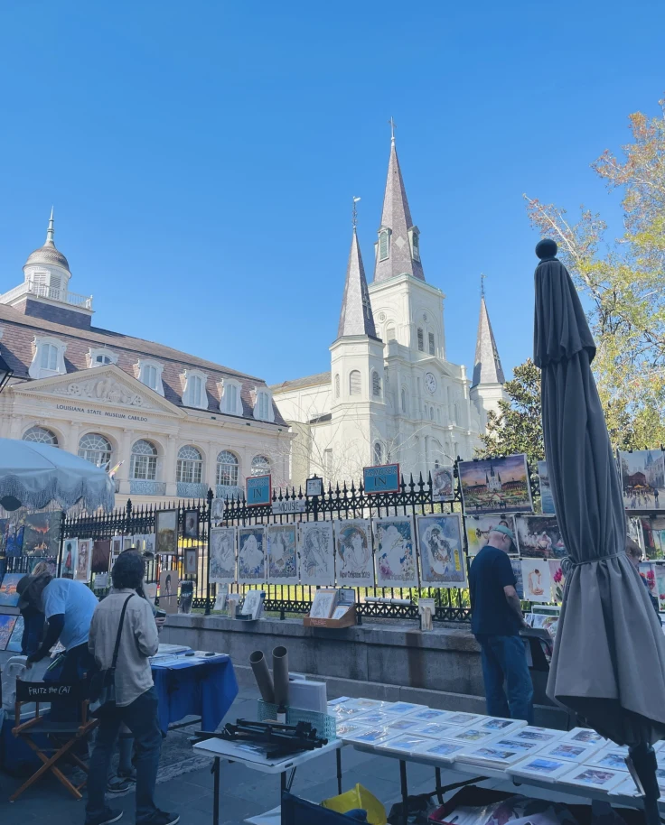 A bottom up view of old architecture, complete with pointed towers and a metal fence. There are also people and umbrellas in the forefront.
