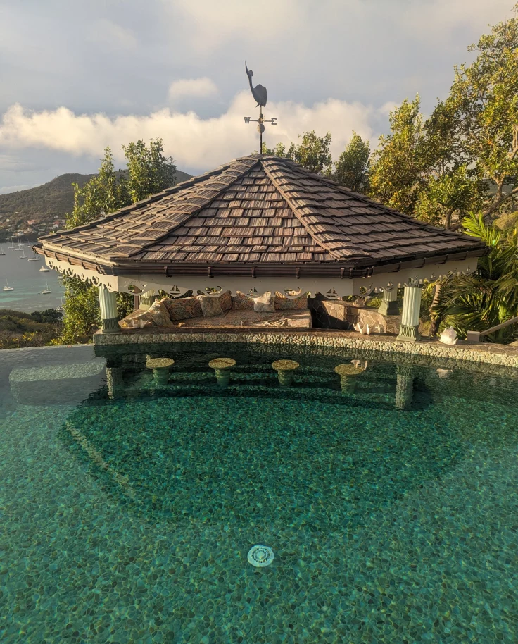 A pool with a seaside hut next to it and a view of the sea and mountains in the distance.