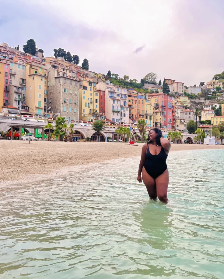 Travel advisor posing in the ocean with a lovely colorful beach town in the distance