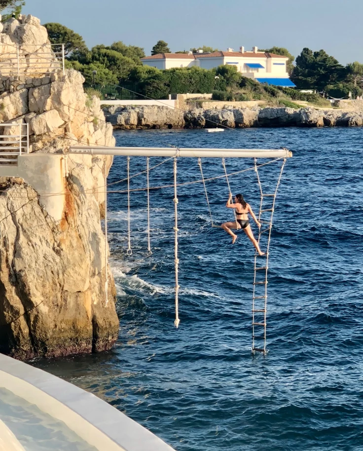 DuCapTrapeze - a woman in a black swimsuit on a ropes course over the sea that is attached to a rocky cliffside