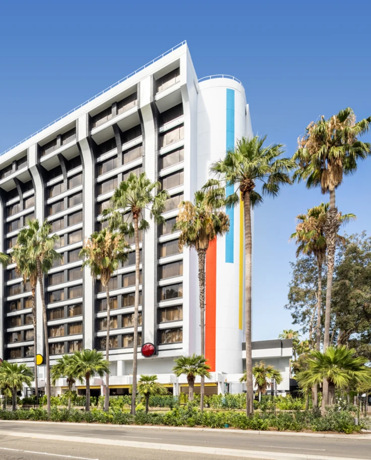 The outside of a white hotel surrounded by palm trees during the daytime
