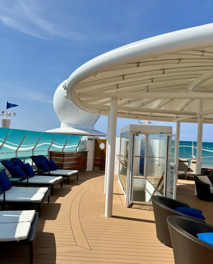 Covered open-air deck on a cruise ship with blue- and white-uphostered chairs.
