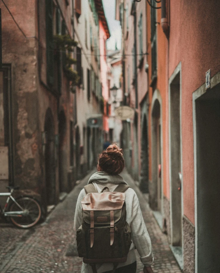 A person wearing a backpack walking down a narrow, cobblestone alley surrounded by colorful, European buildings.