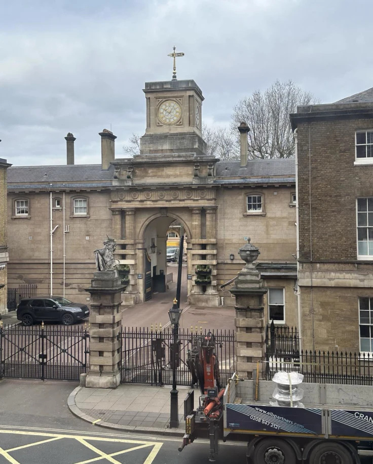 A view of an old stone building closed off with a metal gate and street view in London.