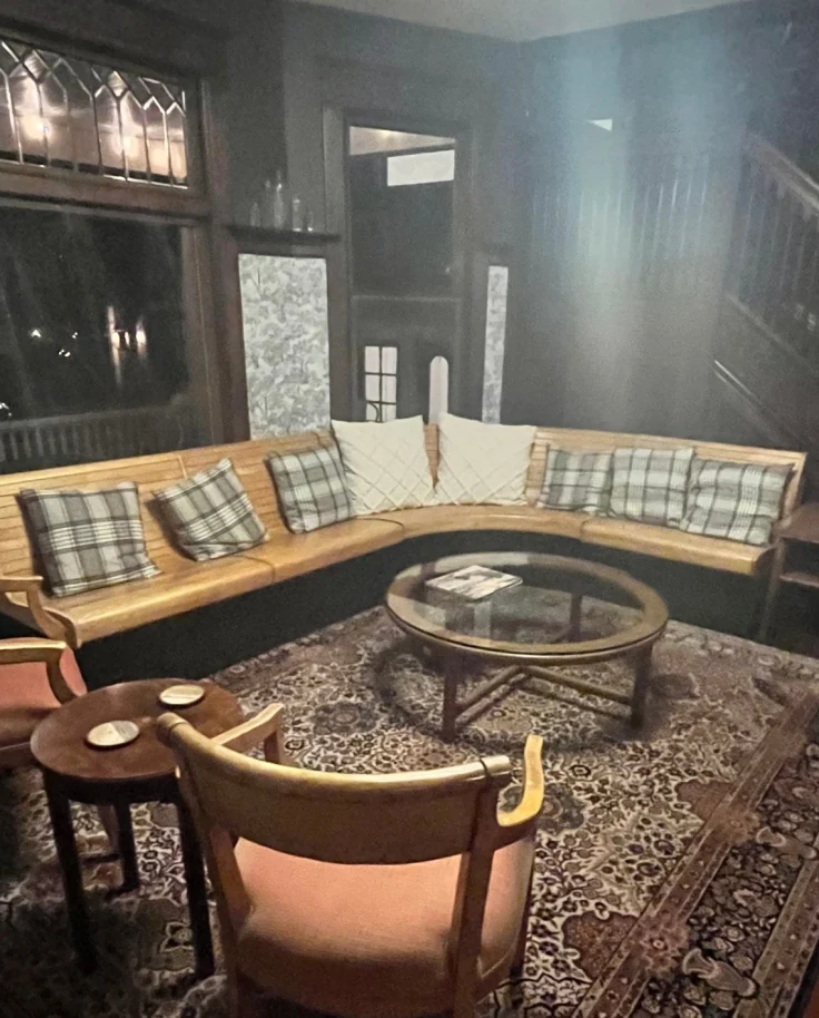 A cozy hotel lobby with plaid pillows on a long leather couch and a Persian rug.