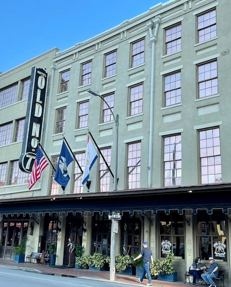 The green exterior of the Old No 77 Hotel in New Orleans with flags flying above the entrance