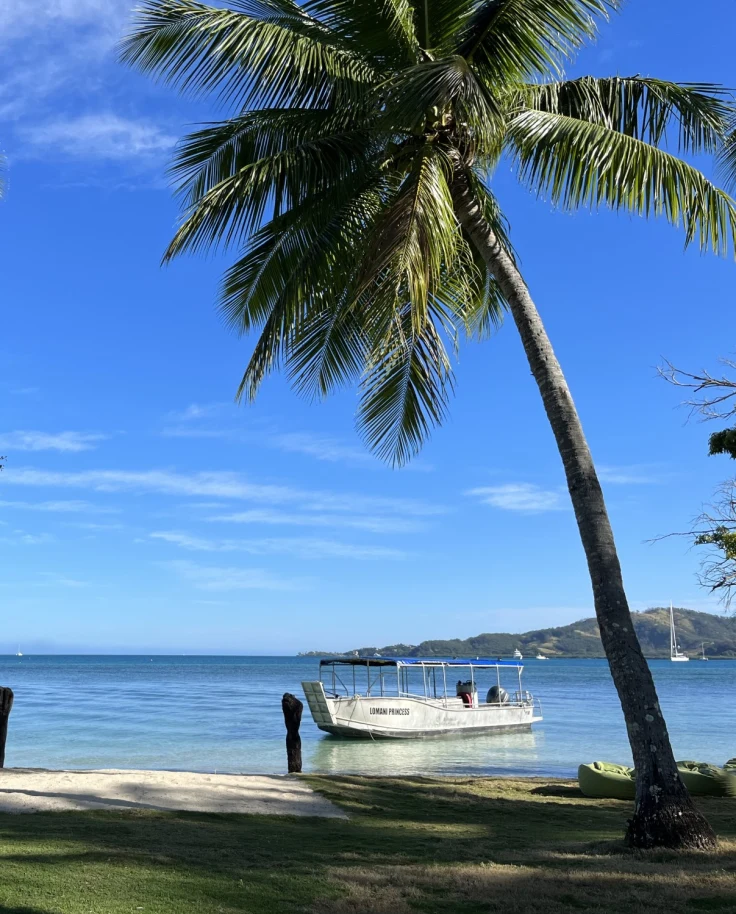 The lawn on the main grounds with palm trees and the ocean in the background with the resort excursion boat, "The Lomani Princess"