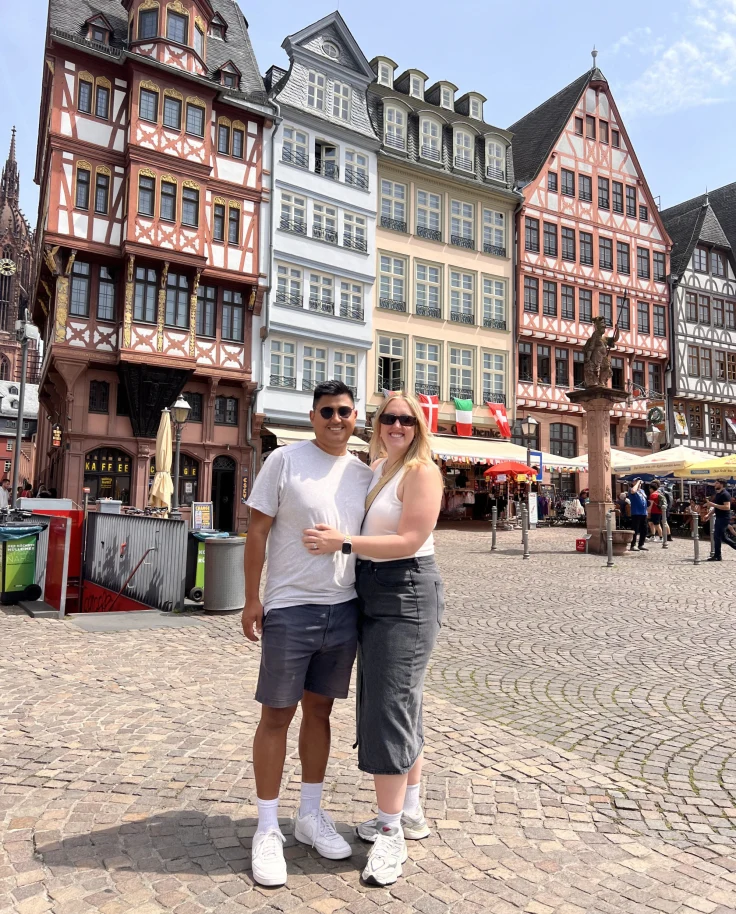 A couple posing for a photograph outside on a city street in front of colorful tall buildings