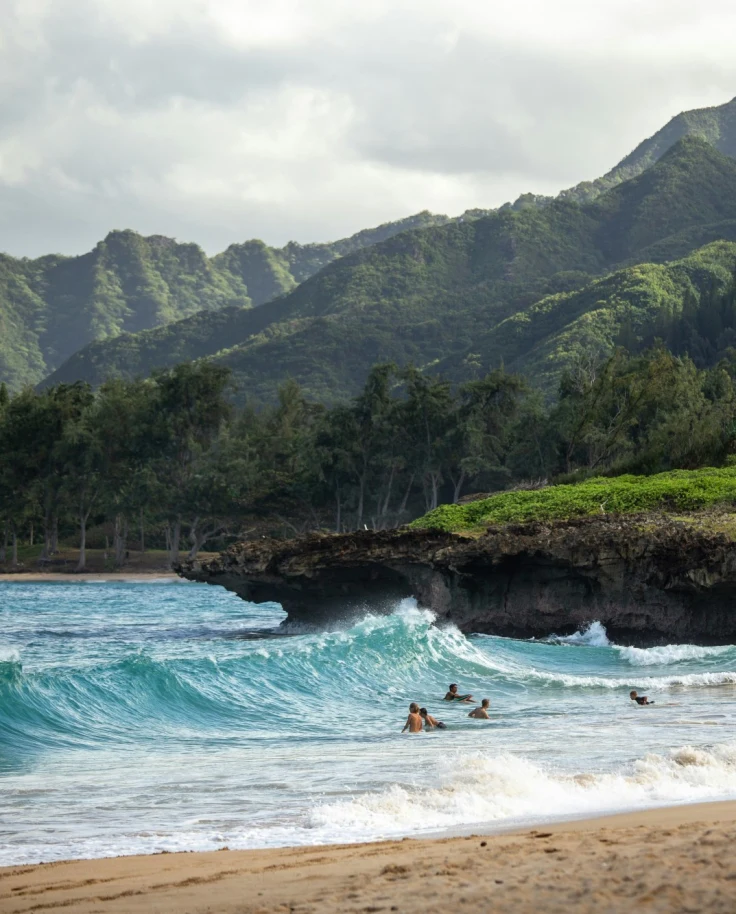 Surfers catching waves by a beach with green mountains in view