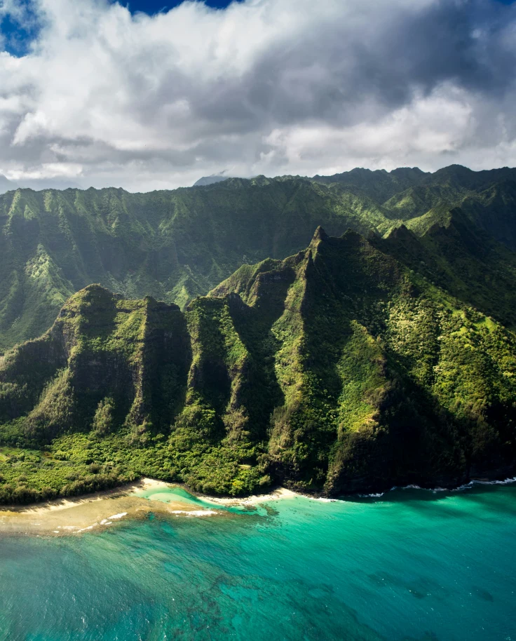 An aerial view of a coastline and green mountains in Hawai'i.