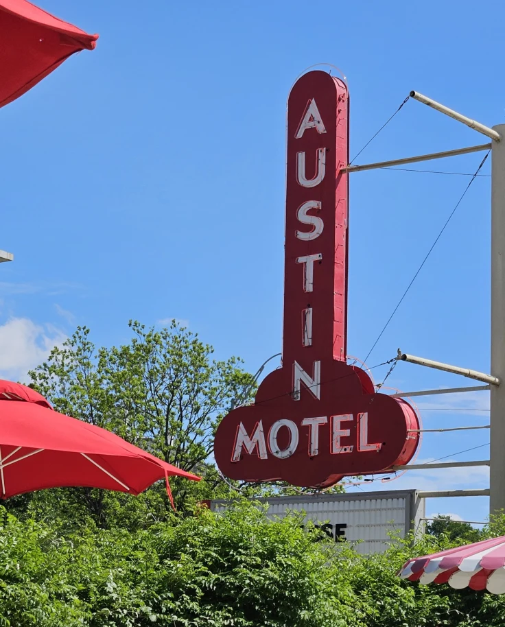 The Austin Motel exterior sign, a red sign near green trees and red umbrellas - Nicole Diez