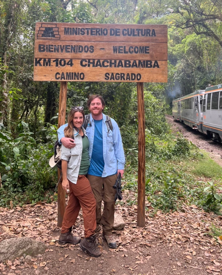 Couple poses in front of a sign in the jungle.