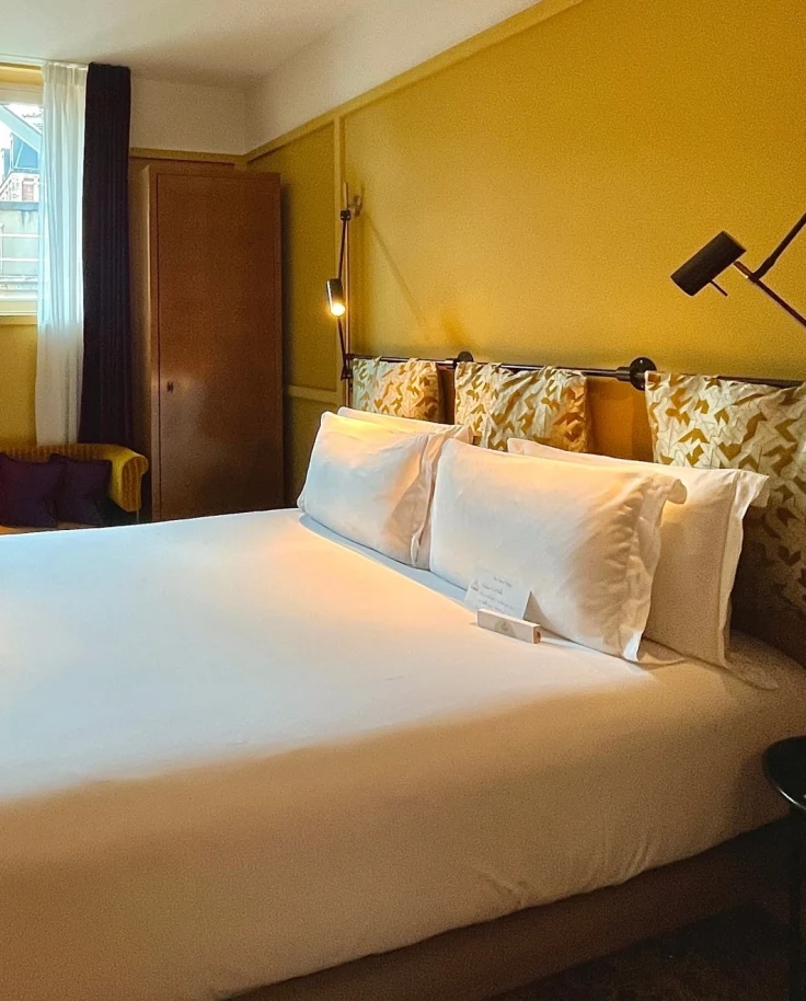 Hotel room with yellow walls and a big bed with white linens.