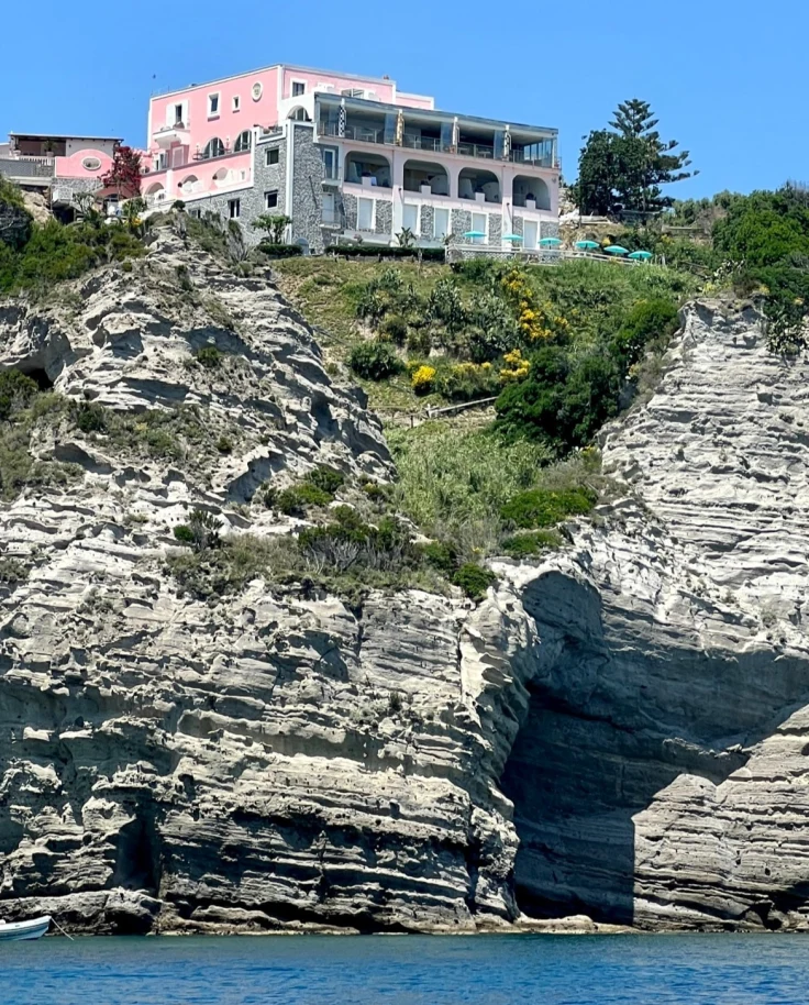 A pink building atop a cliff next to the sea