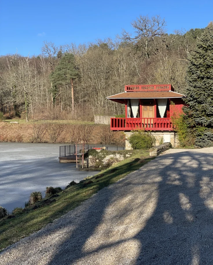A red house in the distance with a concrete road, trees and frozen lake in the surrounding area.