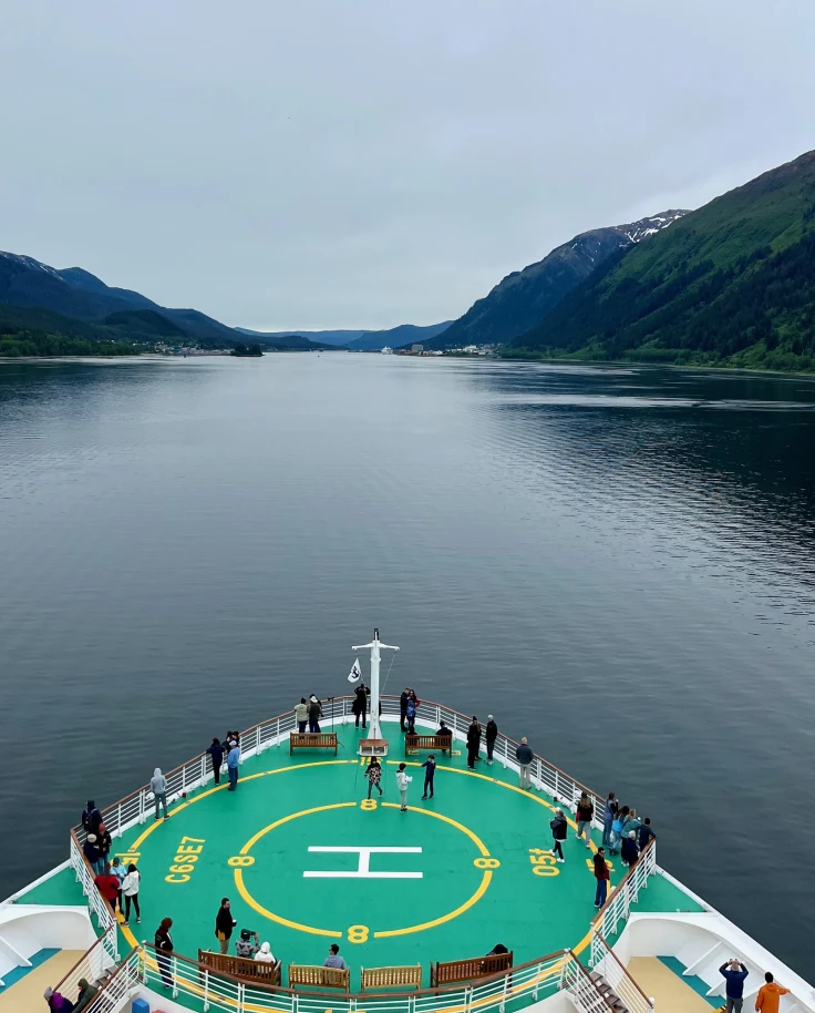 Front deck of a cruise ship on gray waters with high cliffs in the background.
