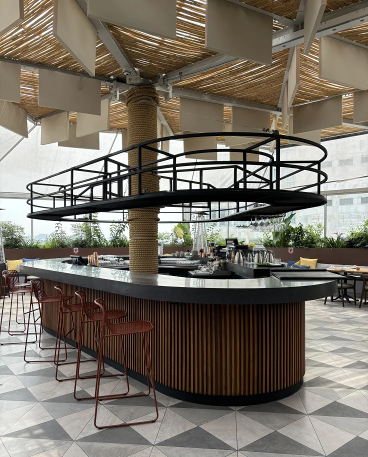A brown and black, modern, oval-shaped bar set in the middle of a spacious and bright restaurant.