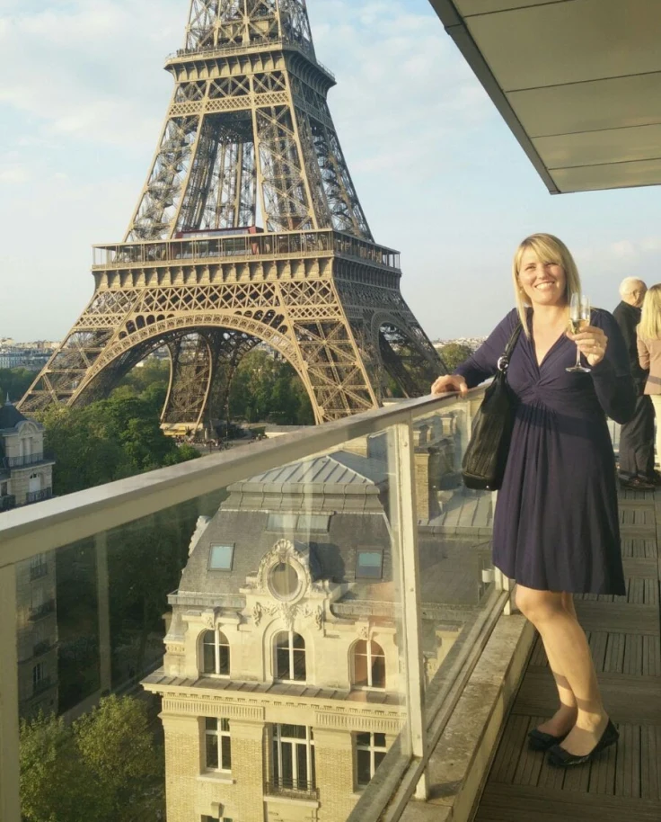Travel advisor Heather in a blue dress standing on a balcony with a glass of champagne and the Eiffel Tower in the background in one of the best areas in Paris.