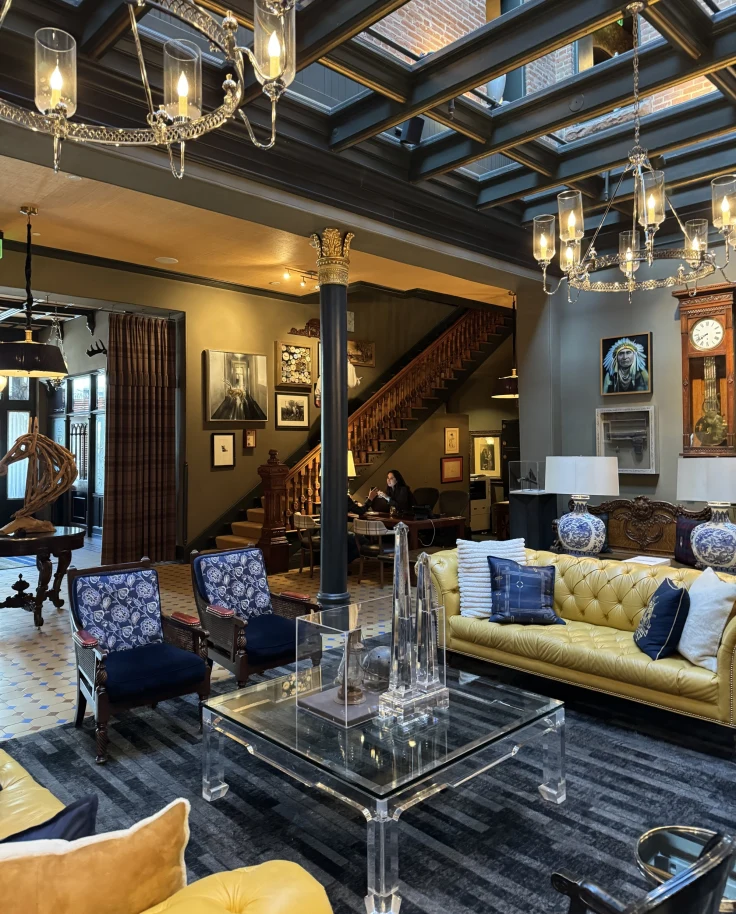 Inside the lobby of the Hotel Jerome, with luxurious couches, sitting chairs, decor, light fixtures and a glass ceiling.