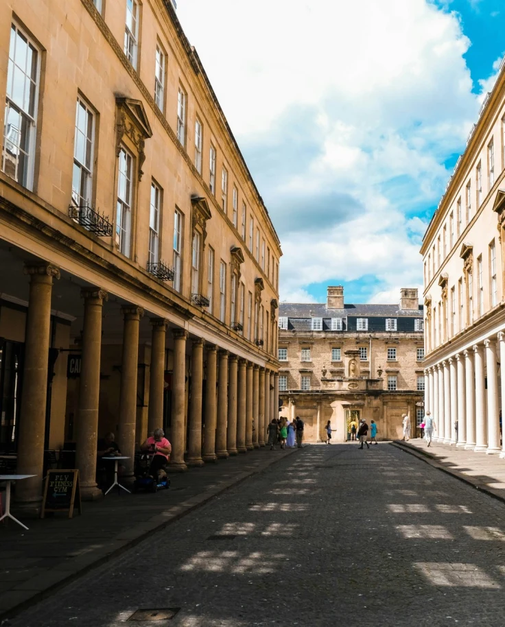 A paved road framed by columned buildings along a shaded corridor of the town on a bright day.