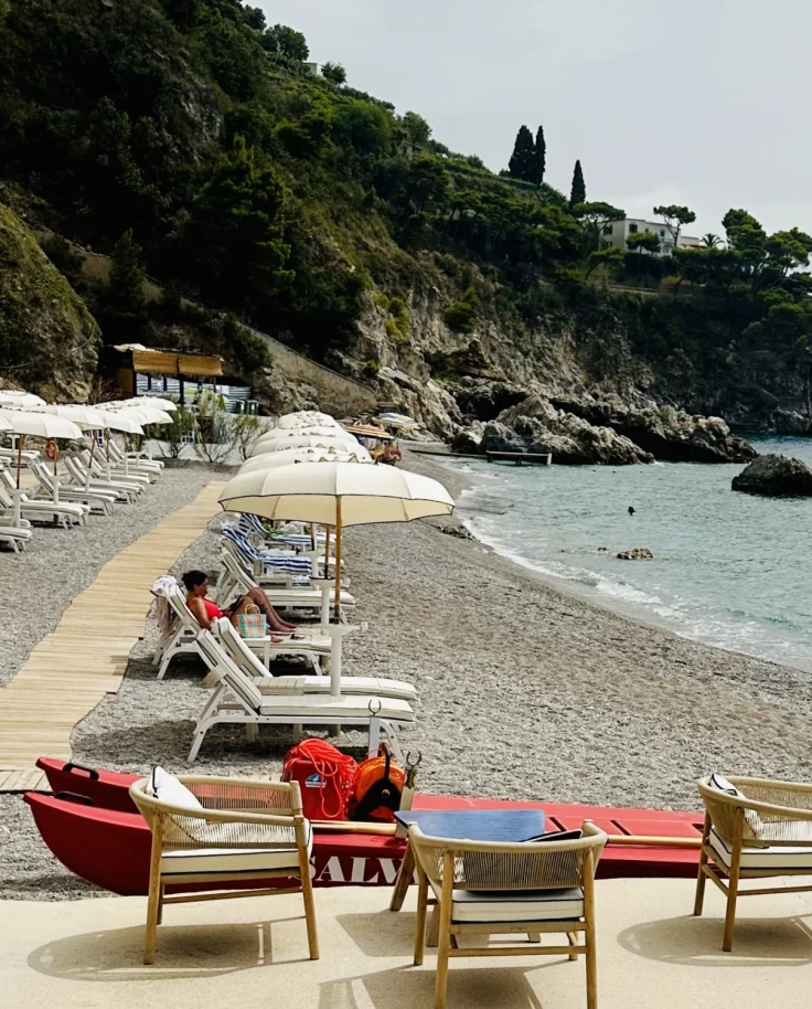 Borgo Sant'Andrea Beach Club on the Amalfi Coast boasts a pristine beach with loungers and umbrellas lining the shore overlooking clear waters on a sunny day.