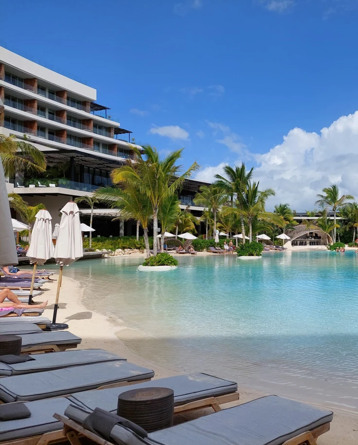 A pool outdoors with blue water and palm trees.