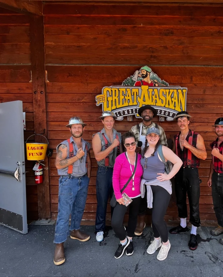 Advisor posing outside the Lumberjack Show with performers on a sunny day.