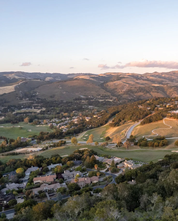 A view of Carmel Valley from above, with rolling hills, a small collection of houses and clouds in the distance - shot by The Nomadic People
