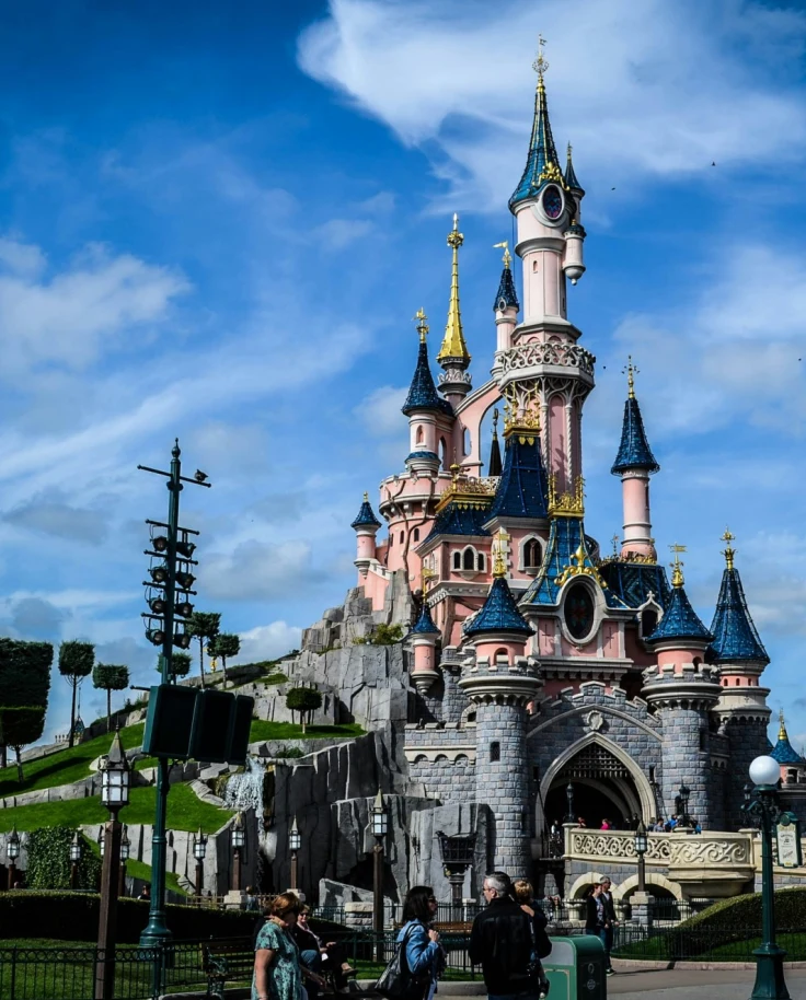 The Disney castle on a grassy hill with blue skies and clouds above it on a beautiful day.