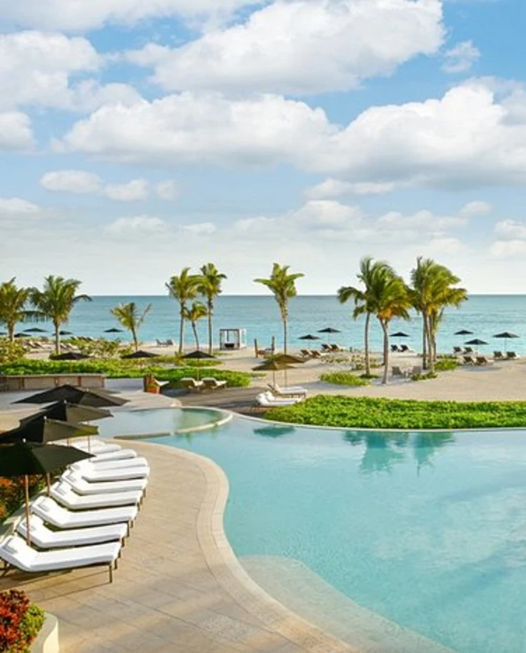 A turquoise pool overlooking a beach with umbrellas and the ocean
