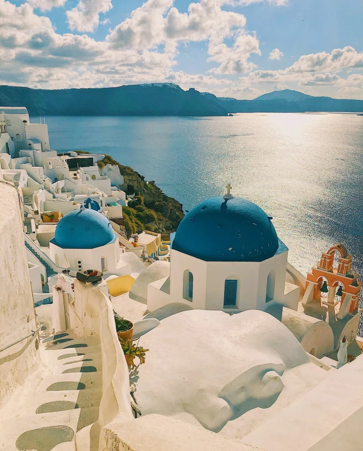 A hillside with white buildings, some with blue dome-shaped roofs, overlooking a beautiful ocean view in Greece