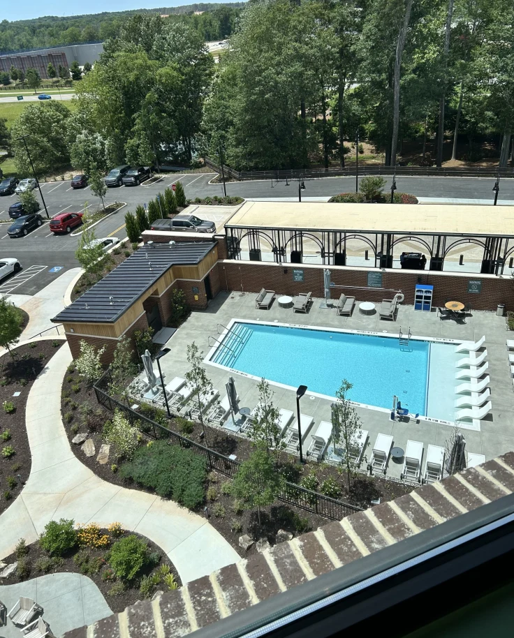 Pool view on a sunny day with foliage and seating.