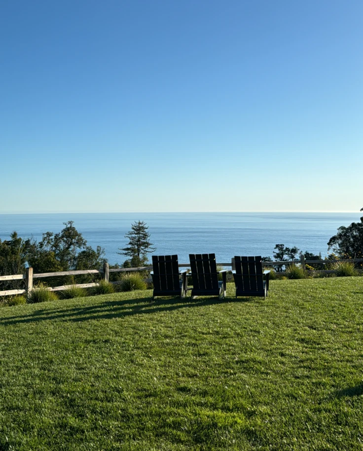 A view of three chairs on a grassy lawn with a view of the blue sea.