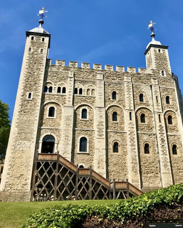 A stone tower in London with grass and tree next to it. The sky is a vibrant blue in the background.