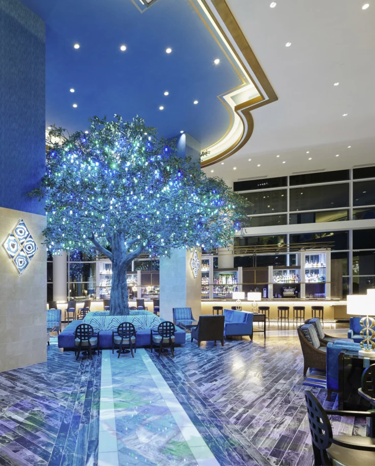 A seating area in a hotel lobby with tall ceilings and lit-up tree in the center