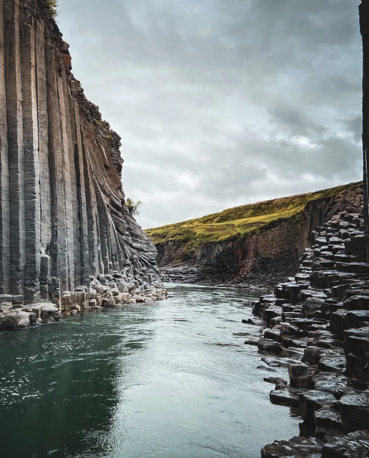 A grey stone cliff in Iceland with a green emerald river flowing through.